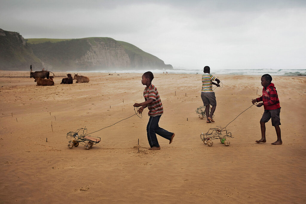 Three African boys with handmade wire cars play on the beach of Coffee Bay, South Africa