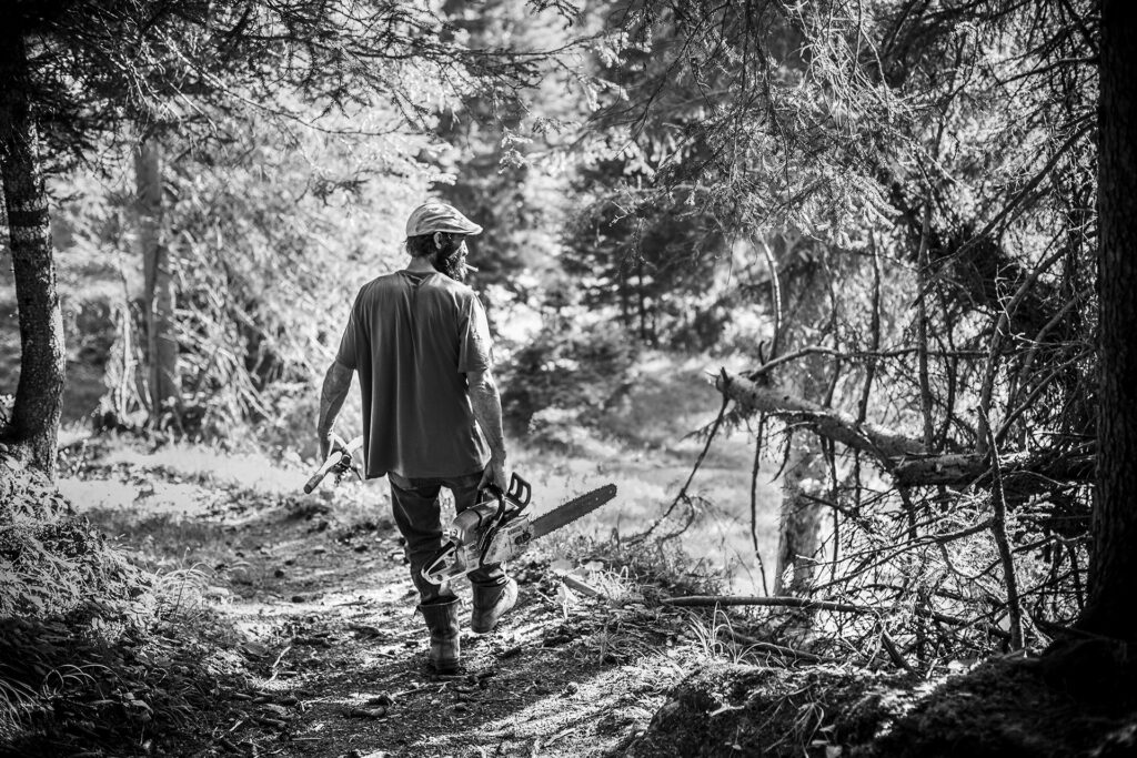 Photo of a man with wood cutting saw walking in the forest Medergen Swiss Alps