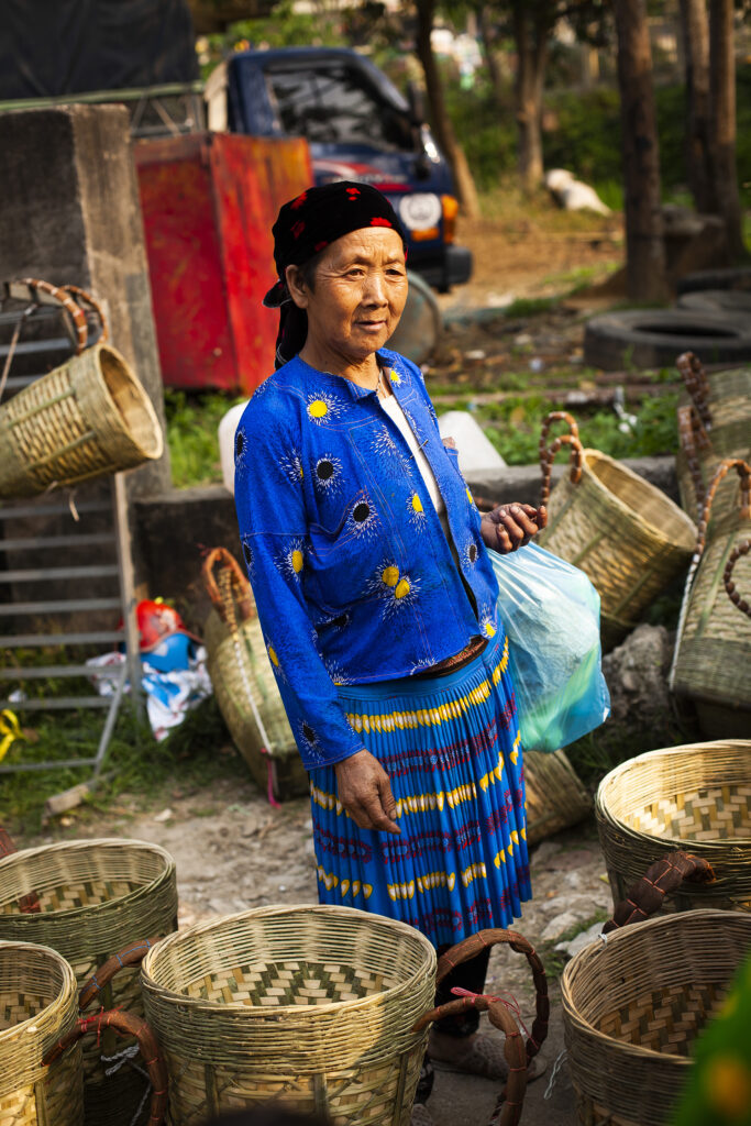 Portrait of a Hmong woman in blue traditional outfit amongst woven baskets.  Vietnam, Ha Giang