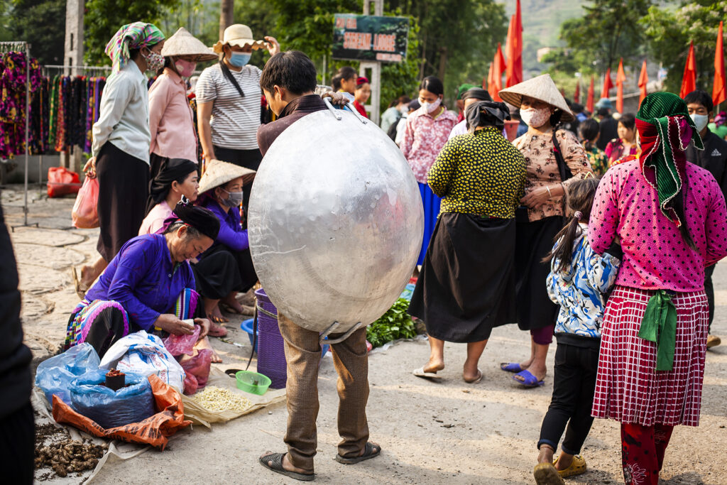 Photo at Hmong market of a man carrying a big wok