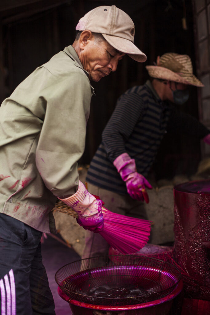 men in process of dipping incense stick in dye
